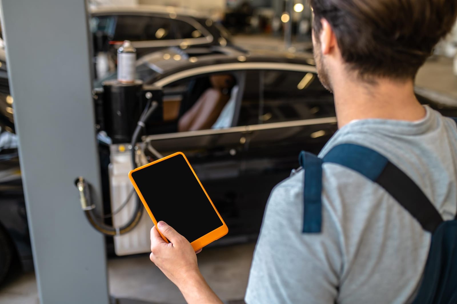 Mecânico segura um tablet enquanto observa um carro em manutenção na oficina.