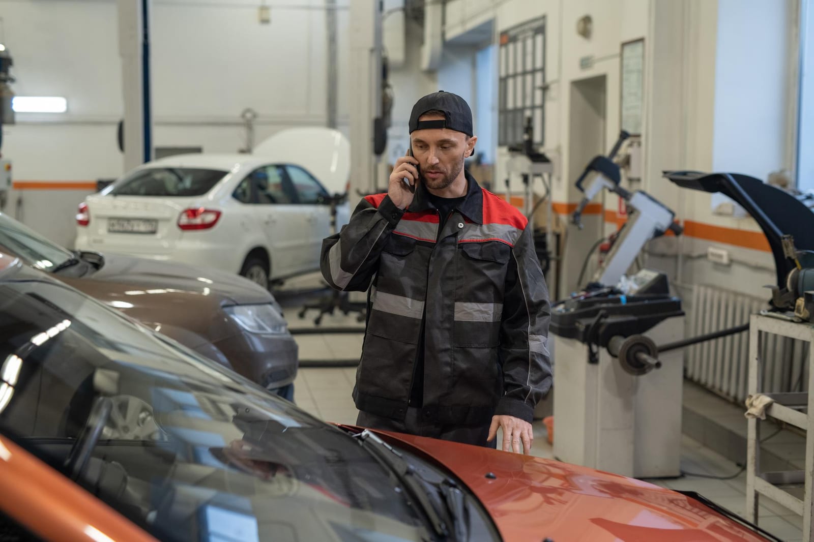 Funcionário de oficina fala ao telefone ao lado de carros em reparo.